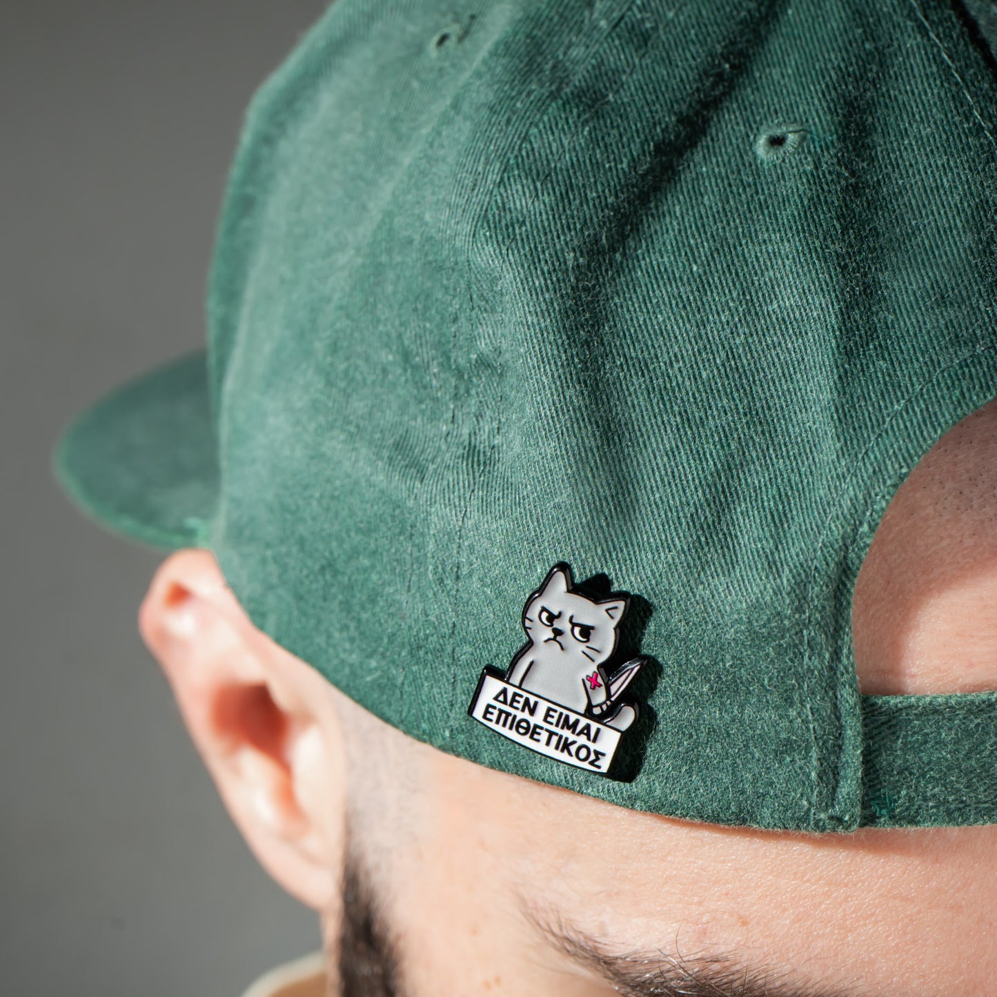 Green cap with a cat-themed enamel pin on the side, featuring text.