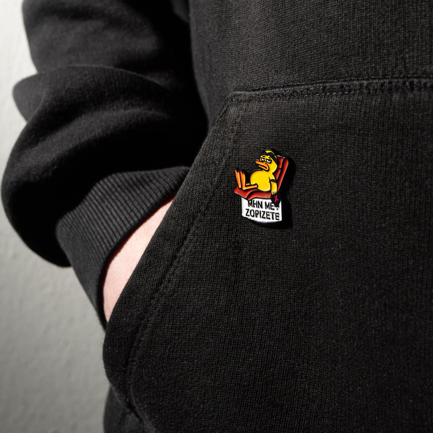 Black hoodie with an enamel pin on the pocket.