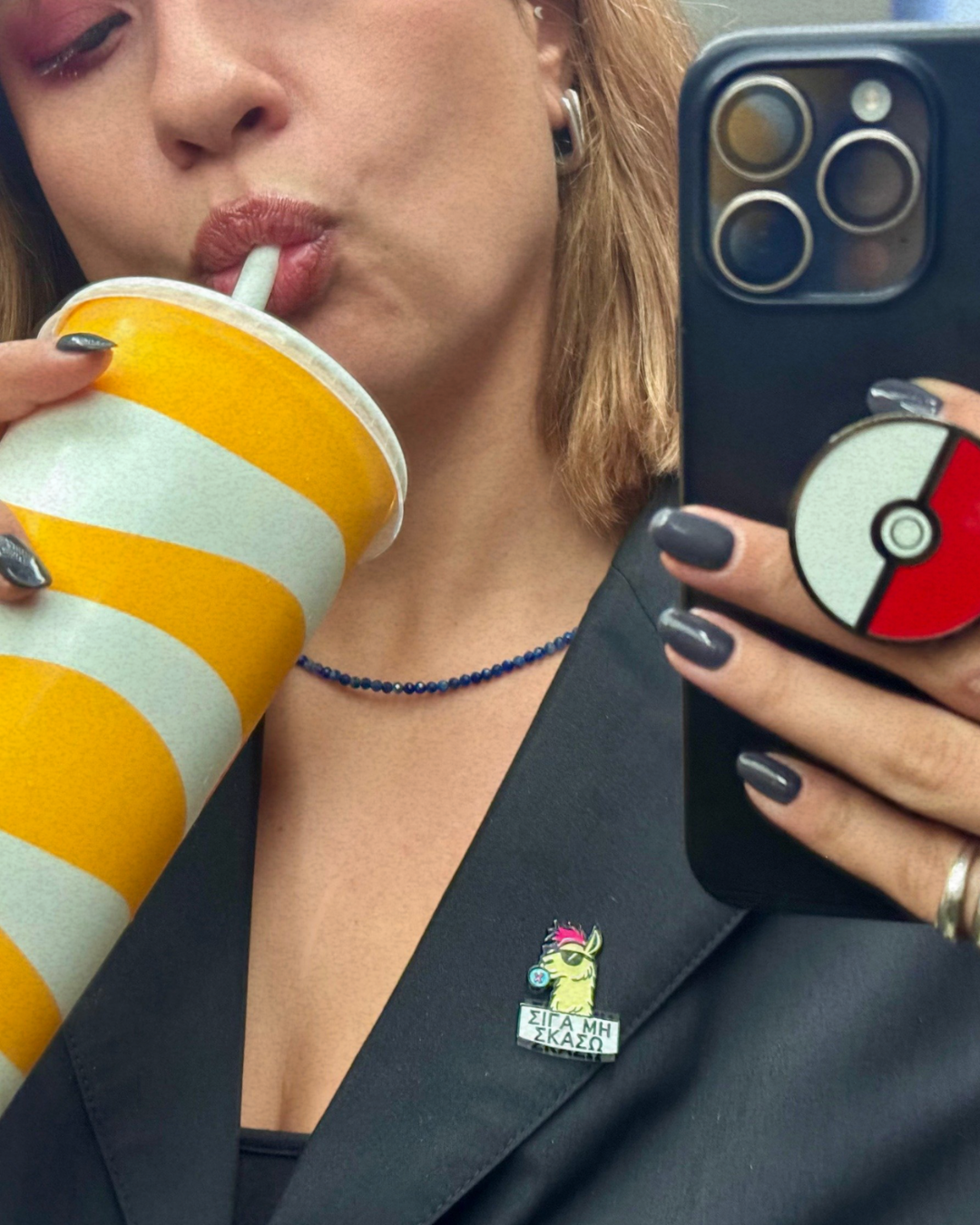 Person drinking from a striped cup and holding a phone with a Poké Ball case.