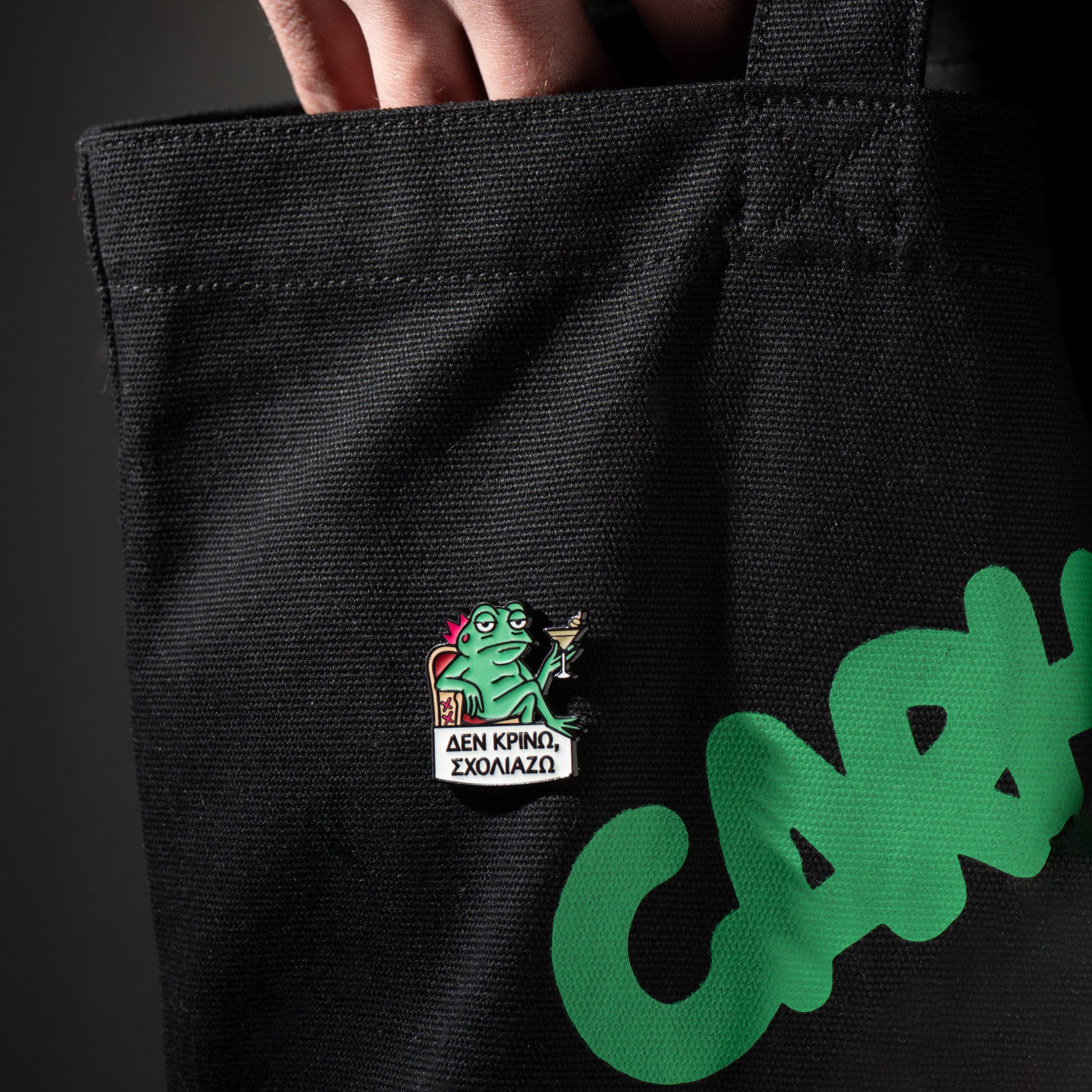 Black tote bag with green text and a frog pin on a dark background