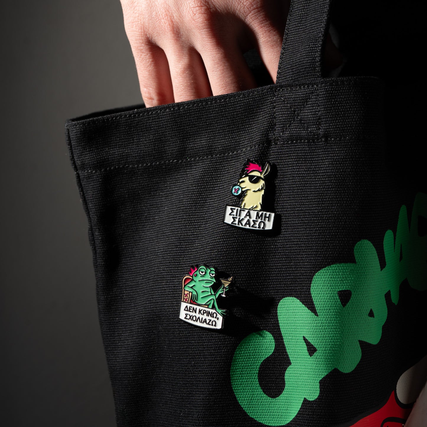 Black tote bag with colorful pins and branding on a dark background