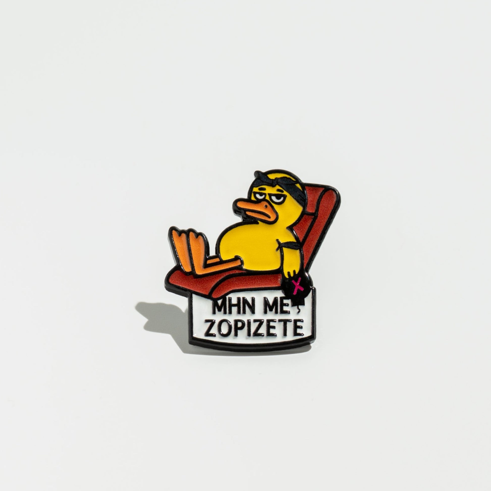 Pin with cartoon duck on a chair and text 'MHN ME ZOPIZETE' on a white background
