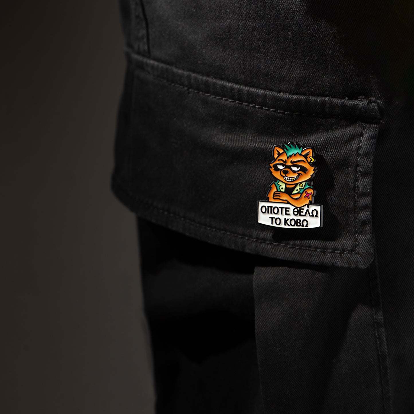 Black cargo pants with a raccoon cartoon character enamel pin on a dark background