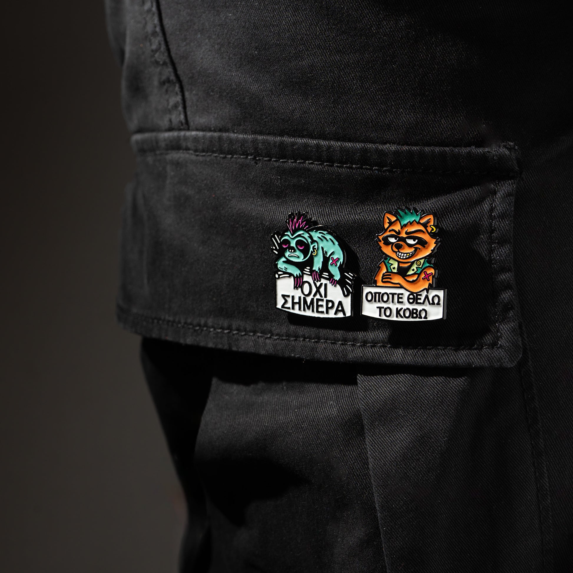 Two colorful enamel pins on a black cargo pants pocket with text and graphics.