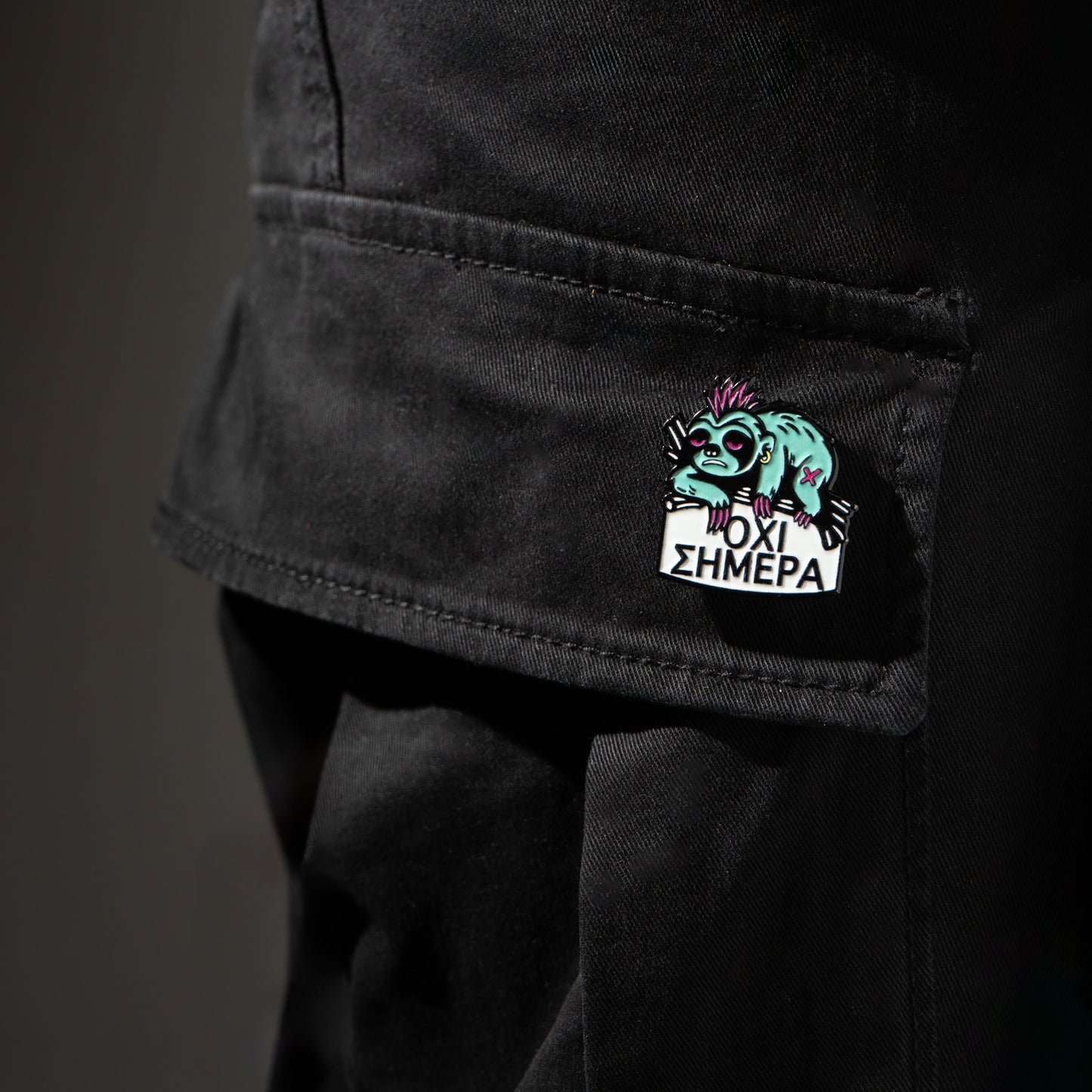 Black pants with a colorful enamel pin sloth on the pocket against a dark background