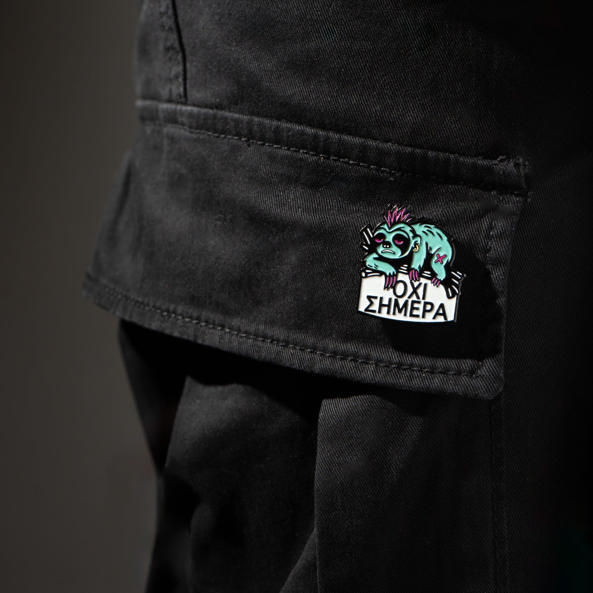 Black pants with a colorful enamel pin sloth on the pocket against a dark background