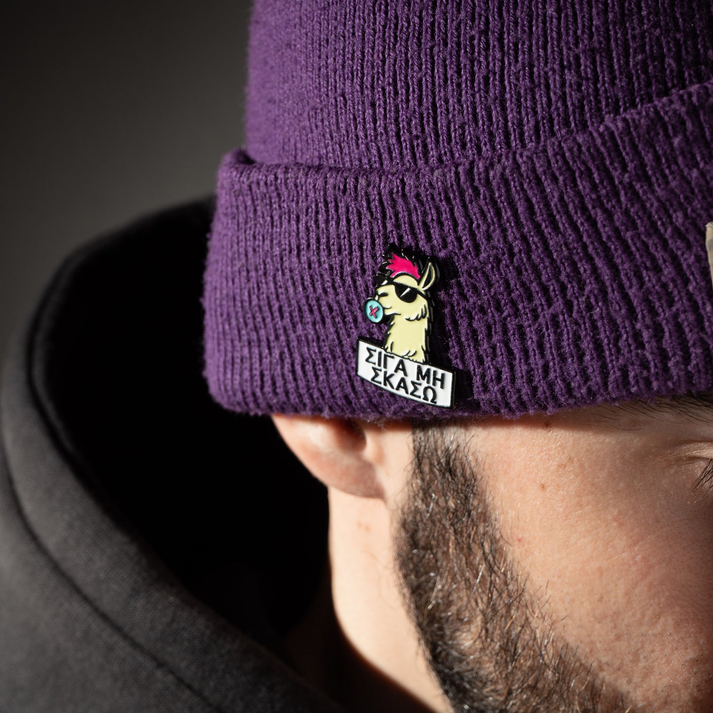 Purple beanie with a cartoon character enamel pin and text on the brim, worn by a person.