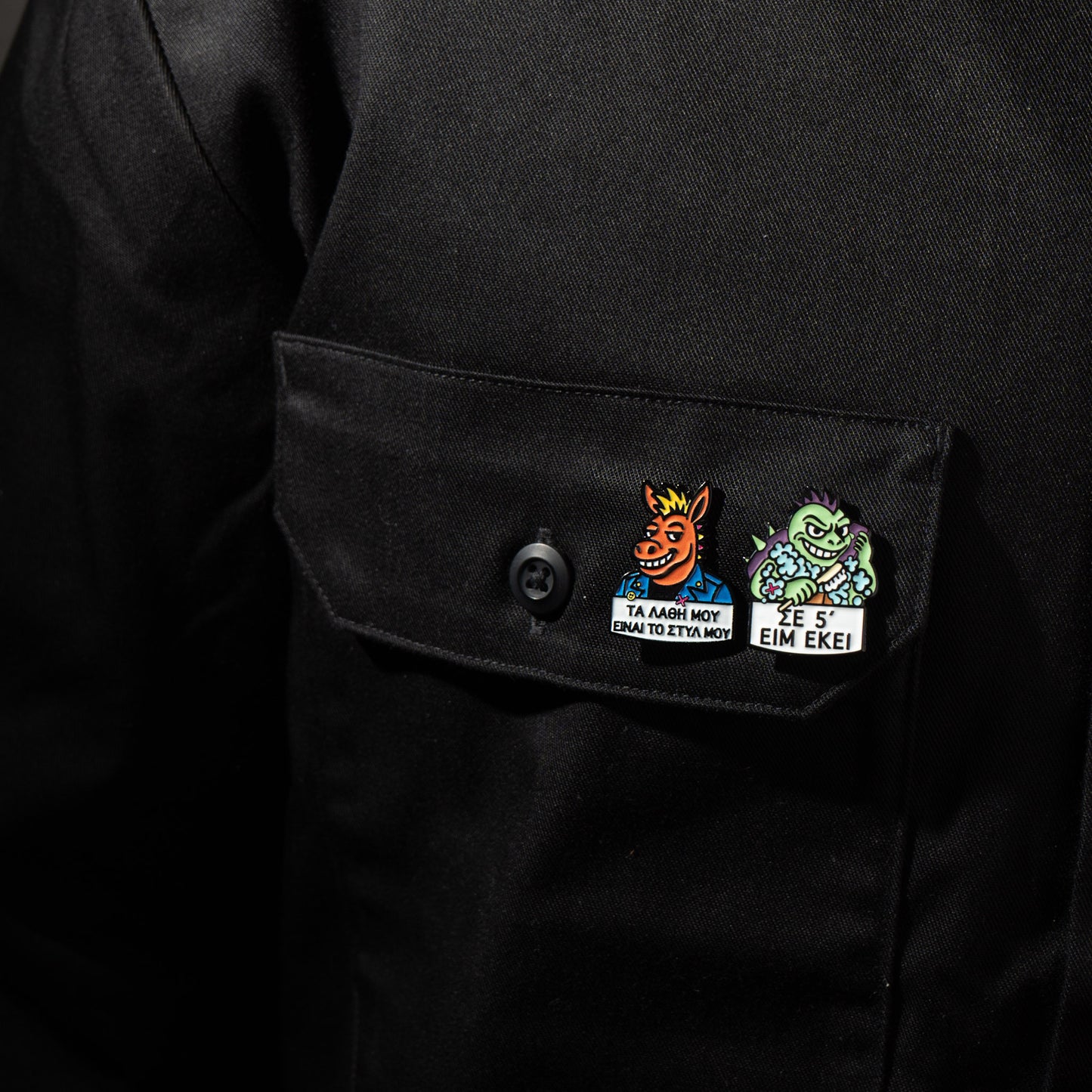Black jacket with two colorful enamel pins on pocket on a dark background
